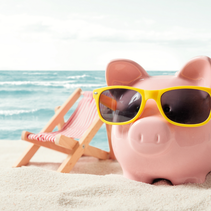 Piggy bank with sunglasses on a beach, next to a beach chair