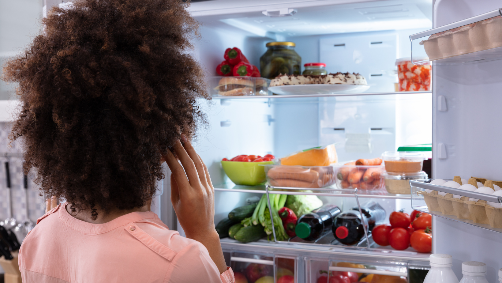 Woman looking at her open, filled fridge